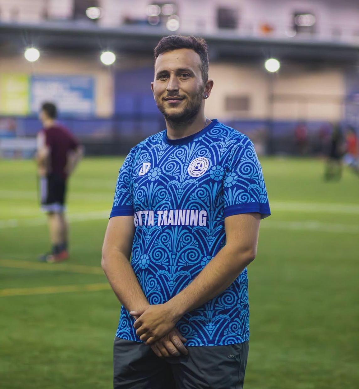 Coach Marko Sinani wearing a blue Betta Training jersey on a soccer field